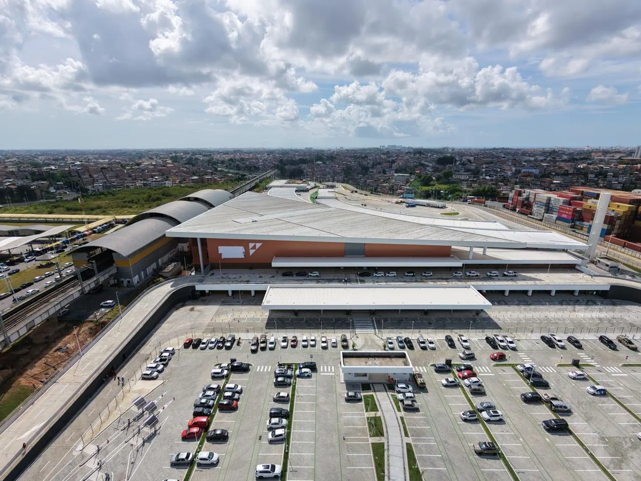 Vista aérea da fachada moderna da Nova Rodoviária de Salvador em Águas Claras, mostrando a passarela de integração com o metrô e a BR-324 ao fundo.