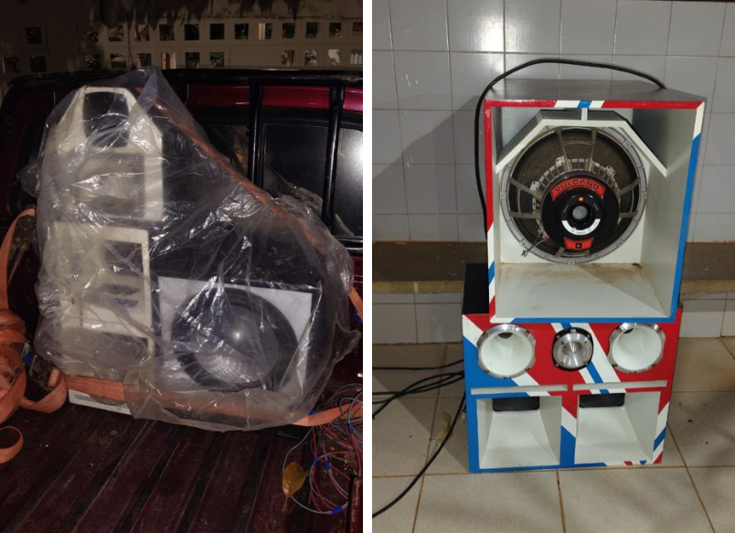 Dois sistemas de som automotivo apreendidos em Livramento de Nossa Senhora: um embalado em plástico na traseira de um veículo, outro pintado com cores vibrantes e posicionado no chão, com alto-falantes visíveis.